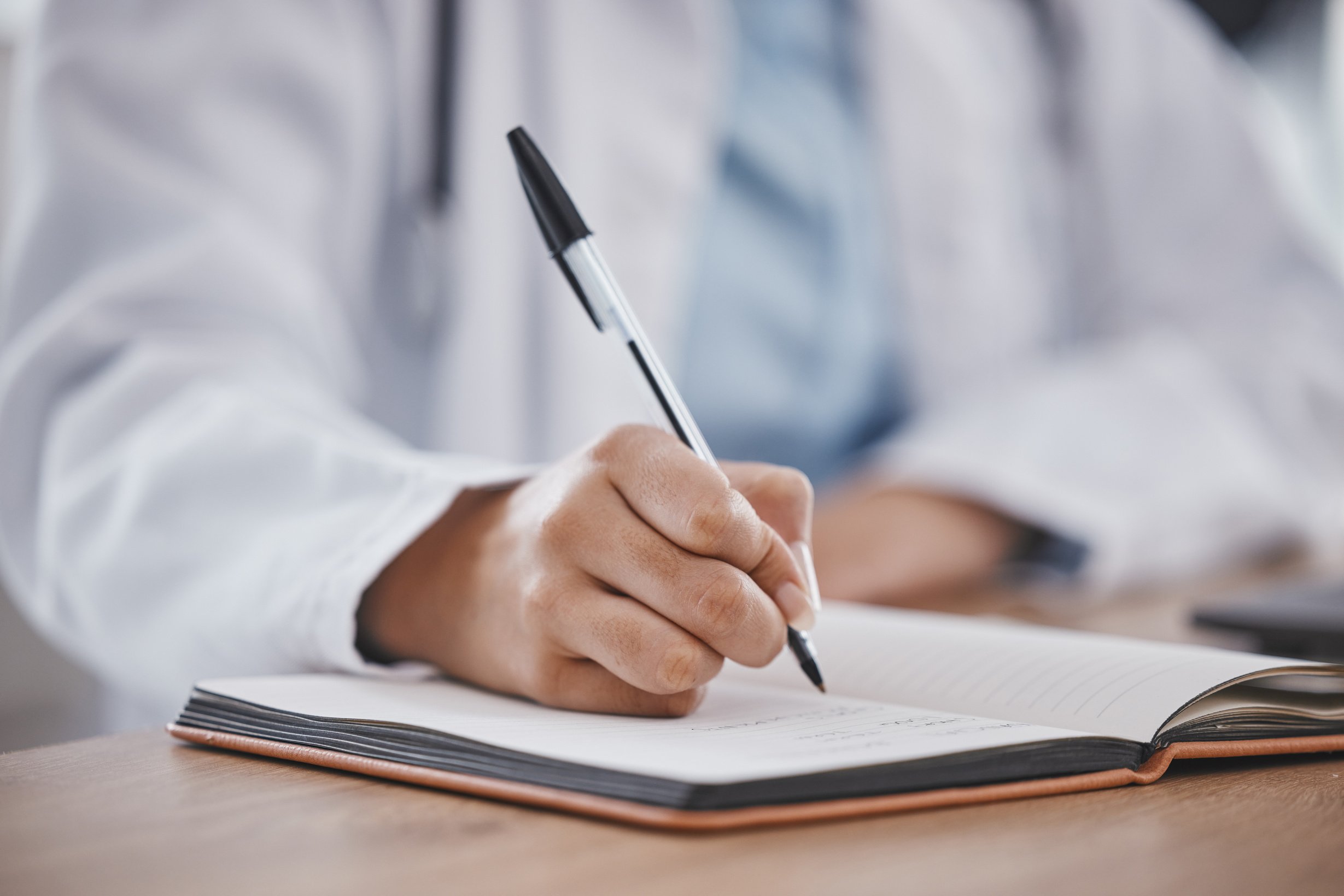 Writing, book and notebook by doctor or healthcare professional with a prescription or making notes in an office. Hand, closeup and medical worker or employee in compliance with schedule